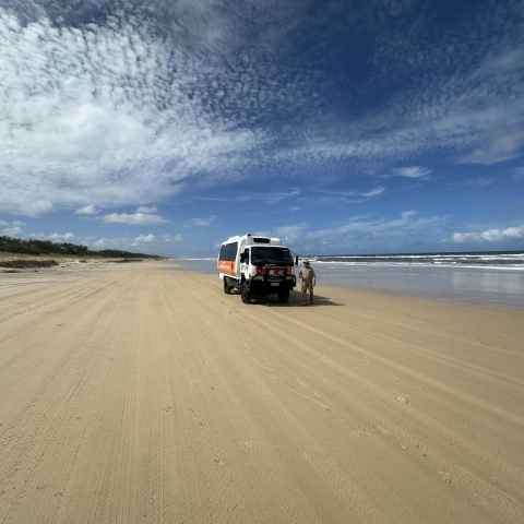 Vehicle on a sandy beach under a partly cloudy sky.