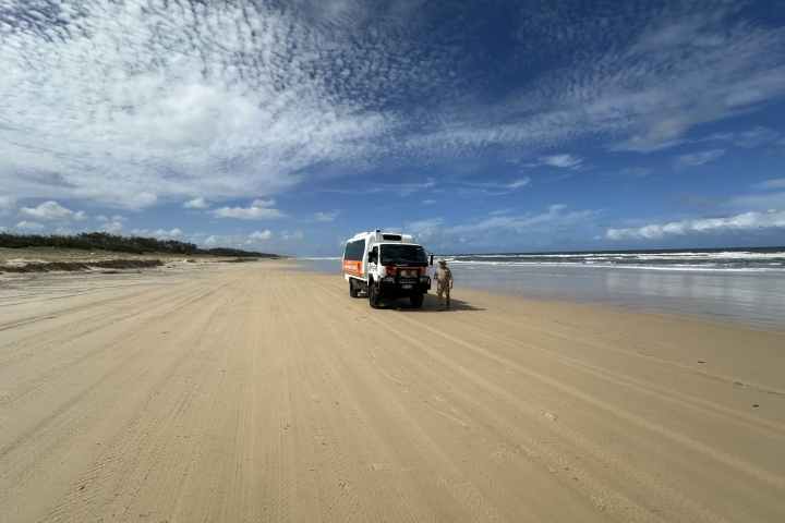 Vehicle on a sandy beach under a partly cloudy sky.