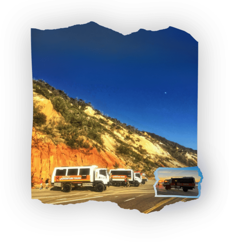 Vans parked on a desert road with a rocky hill in the background.