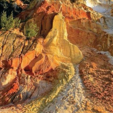 Colorful rock formation with orange, red, and yellow hues, with sparse vegetation on top.
