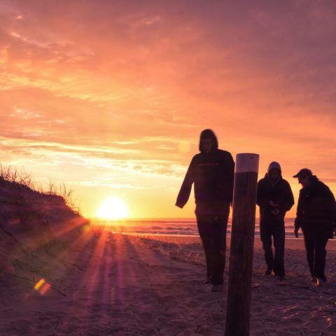 Three people walking on a beach at sunrise with colorful sky.