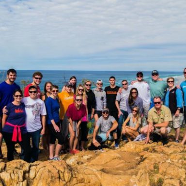 Group of people posing on rocky ground with ocean in the background.