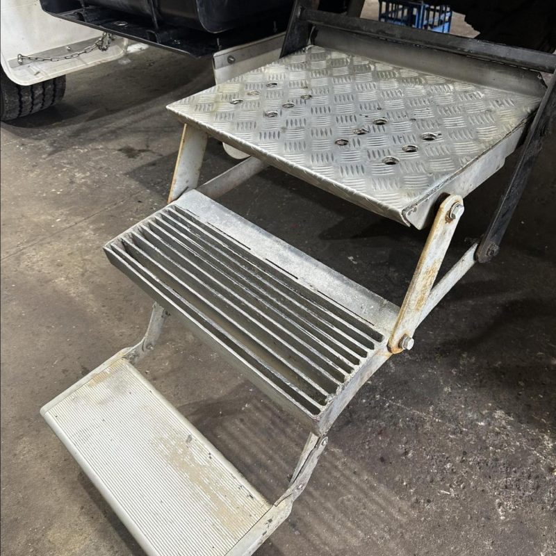 Metallic folding steps with textured surfaces on a concrete floor.